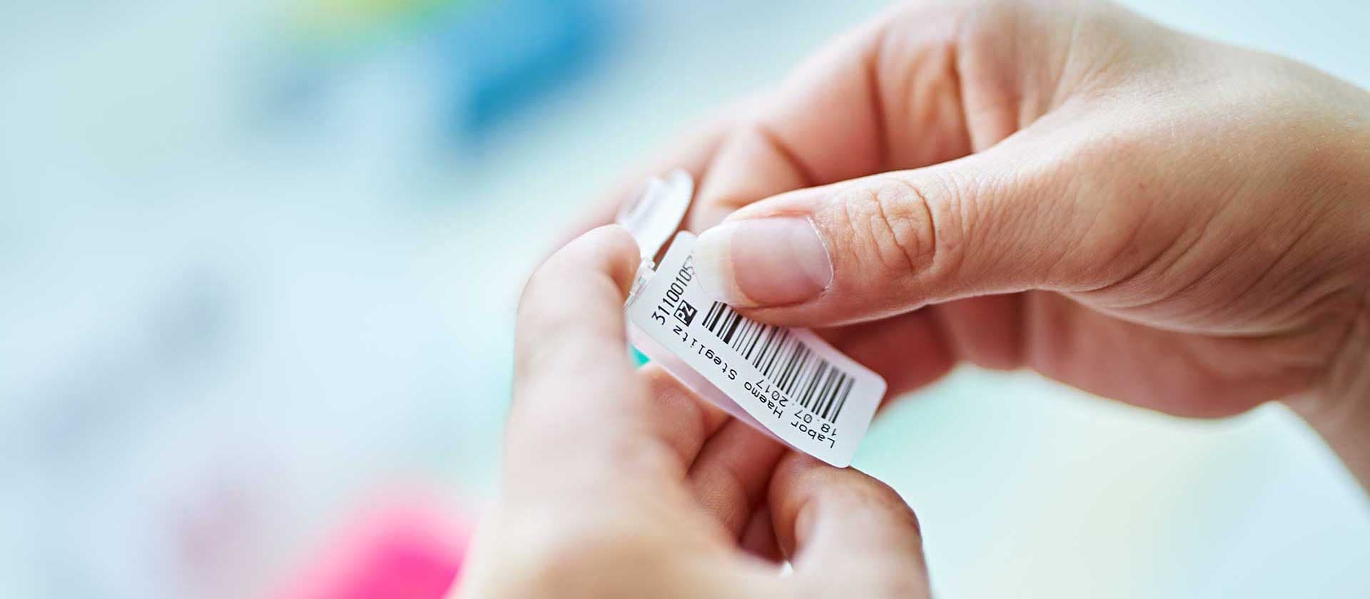 Person hält eine beschriftete Probeflasche mit einem Barcode-Etikett im IHP-Labor.